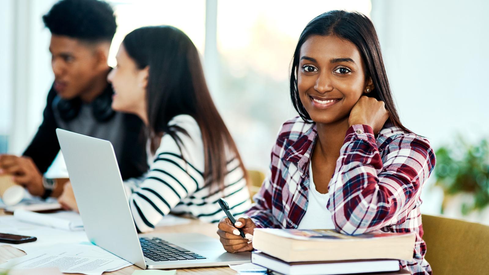 oung woman with laptop and textbooks, with her fellow students in the background